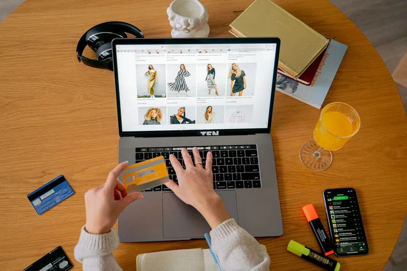 Une cliente parcourt une boutique de mode en ligne sur son ordinateur portable, une carte bancaire à la main